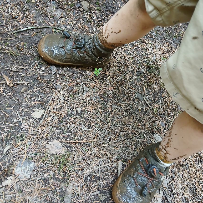 Ein Nahaufnahme von einem Kindes schlammigen Schuhen und Beinen, die den Schmutz und das Gras auf dem Boden zeigen.
