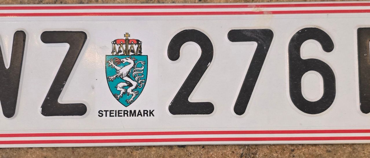 Ein weißer Nummernschild mit roten Rändern zeigt die Nummer 27. Es hat einen blauen Schild mit einem weißen Löwenwappen und einer roten Krone darüber, beschriftet mit 'TIERMARK'.