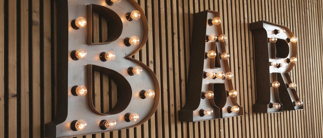 Das Wort Bar ist auf einer Holzwand mit großen Metallbuchstaben angebracht, jeder Buchstabe hat eine Reihe kleiner Lichter im Inneren.