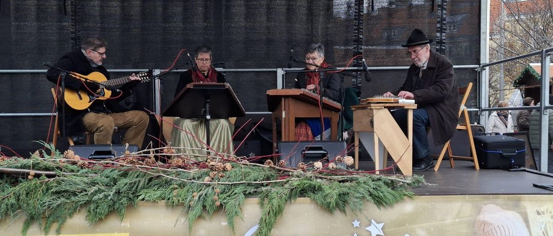 Eine Gruppe von Musikern tritt während des Advents in Wiener Neustadt auf der Bühne auf. Sie spielen verschiedene Instrumente.