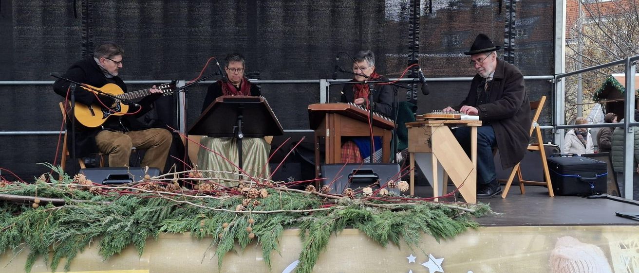 Eine Gruppe von Musikern tritt während des Advents in Wiener Neustadt auf der Bühne auf. Sie spielen verschiedene Instrumente.