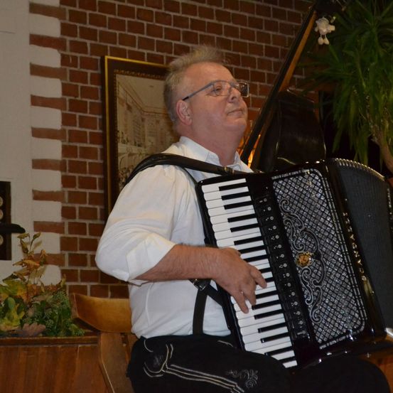Bild enthält, Plant, Potted Plant, Planter, Adult, Male, Man, Person, Glasses, Musical Instrument, Accordion