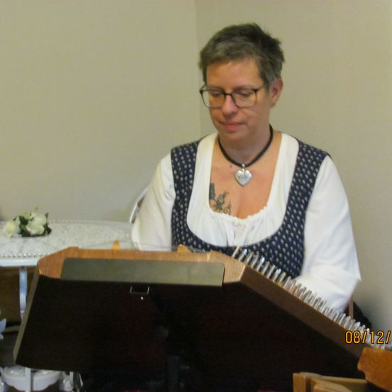 Bild enthält, Plywood, Wood, Person, Flower, Flower Arrangement, Plant, Face, Head, Glasses, Musical Instrument