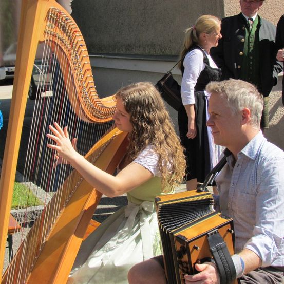 Eine junge Frau spielt Harfe, während ein älterer Mann Akkordeon spielt. Sie treten draußen auf.