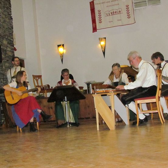 Eine Gruppe von Musikern tritt auf der Bühne auf, eine Frau spielt Gitarre, andere spielen Akkordeon und ein Mann liest Noten.