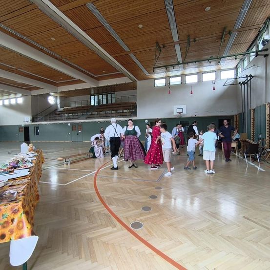 Eine Gruppe von Menschen tanzt in einer Turnhalle mit Holzboden und einem Basketballkorb.