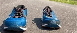 Ein Paar blaue Laufschuhe mit braunen Schnürsenkeln liegt auf einer asphaltierten Straße mit grünem Gras an den Seiten.