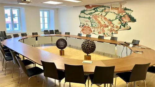 Ein Konferenzraum mit einem großen ovalen Tisch, Stühlen und einem Wandbild. Zwei kugelförmige Objekte stehen auf dem Tisch.