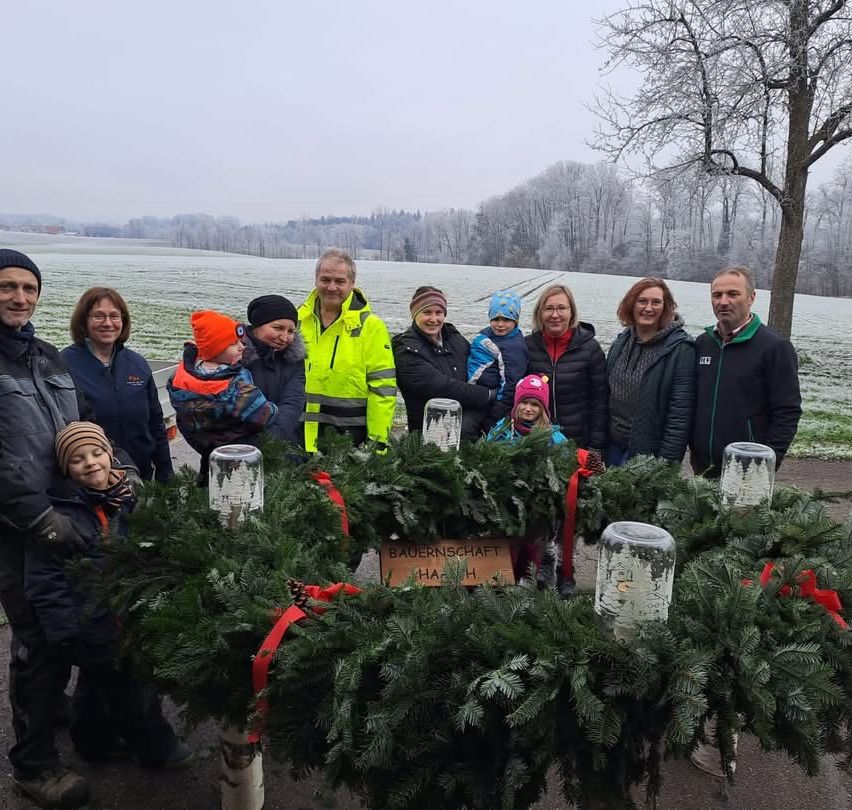 Eine Gruppe von Menschen in Winterkleidung posiert für ein Foto vor dekorierten Kränzen. Ein verschneite Landschaft ist im Hintergrund zu sehen.