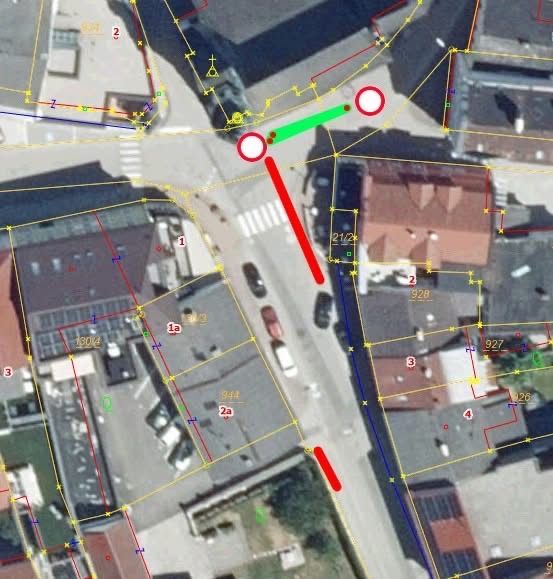 Eine Luftaufnahme zeigt eine Straße mit Gebäuden, geparkten Autos und einem markierten Fußgängerüberweg mit roten und grünen Linien. Zahlen und Buchstaben zeigen verschiedene Abschnitte an.