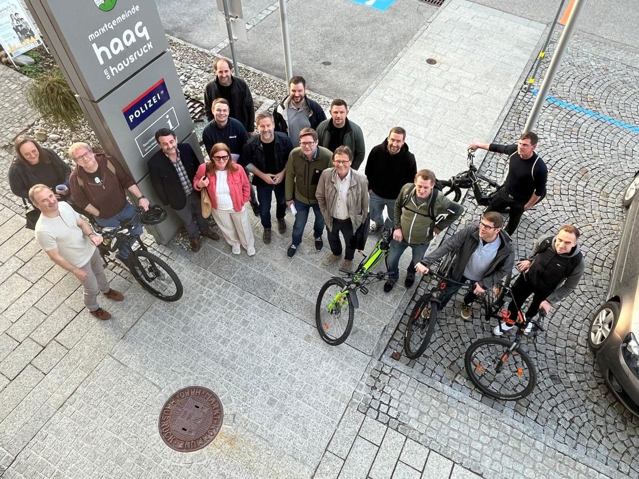 Eine Gruppe von Menschen steht auf einem Bürgersteig neben einem Schild für die Polizei. Sie tragen alle Brillen, Schuhe und halten Fahrräder. Einige von ihnen tragen Jacken und Hosen. Sie halten wahrscheinlich eine Versammlung ab.