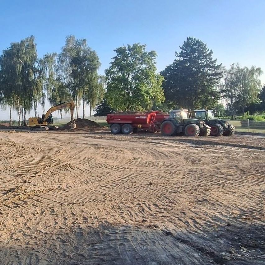 Eine Baustelle mit einem gelben Bagger, einem roten Kipplaster und zwei grünen Traktoren, die auf einem Erdfeld mit Reifenspuren unter einem klaren blauen Himmel geparkt sind.