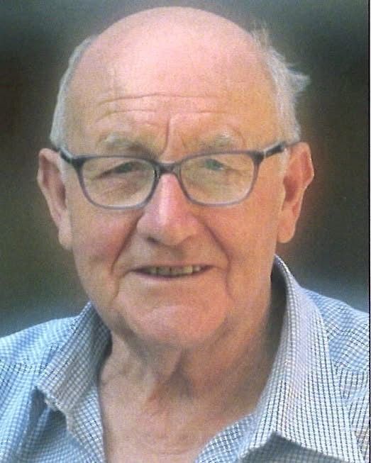 Ein älterer Mann mit kahlem Kopf, Brille und blauem kariertem Hemd, lächelt leicht.