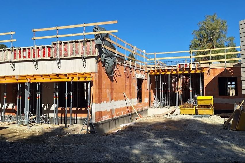Eine Baustelle mit einem im Bau befindlichen Gebäude, mit Ziegelwänden, Holzgerüst und gelben Lagerboxen.