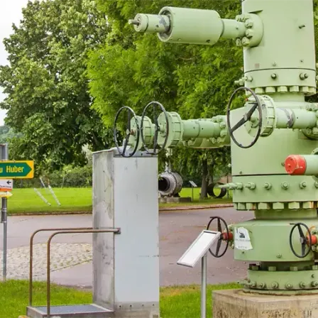 Eine alte industrielle Pumpe im Freien ausgestellt. Sie hat mehrere Ventile und Rohre, grün gestrichen, und steht auf einem Betonblock. Ein Schild ist in der Nähe sichtbar.