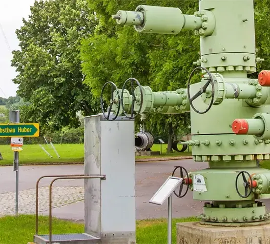 Eine alte industrielle Pumpe im Freien ausgestellt. Sie hat mehrere Ventile und Rohre, grün gestrichen, und steht auf einem Betonblock. Ein Schild ist in der Nähe sichtbar.