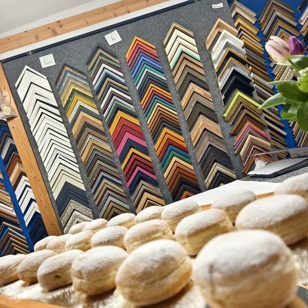 Eine Reihe bunter Bilderrahmen an einer Wand, mit puderzuckerüberzogenen Donuts, die auf einem Tablett im Vordergrund angeordnet sind.