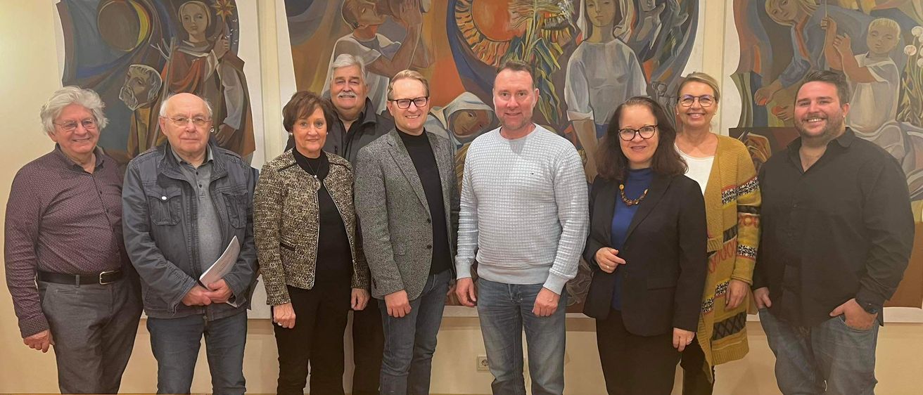 Eine Gruppe von Menschen steht lächelnd vor einer Wand mit großen Gemälden für ein Foto.