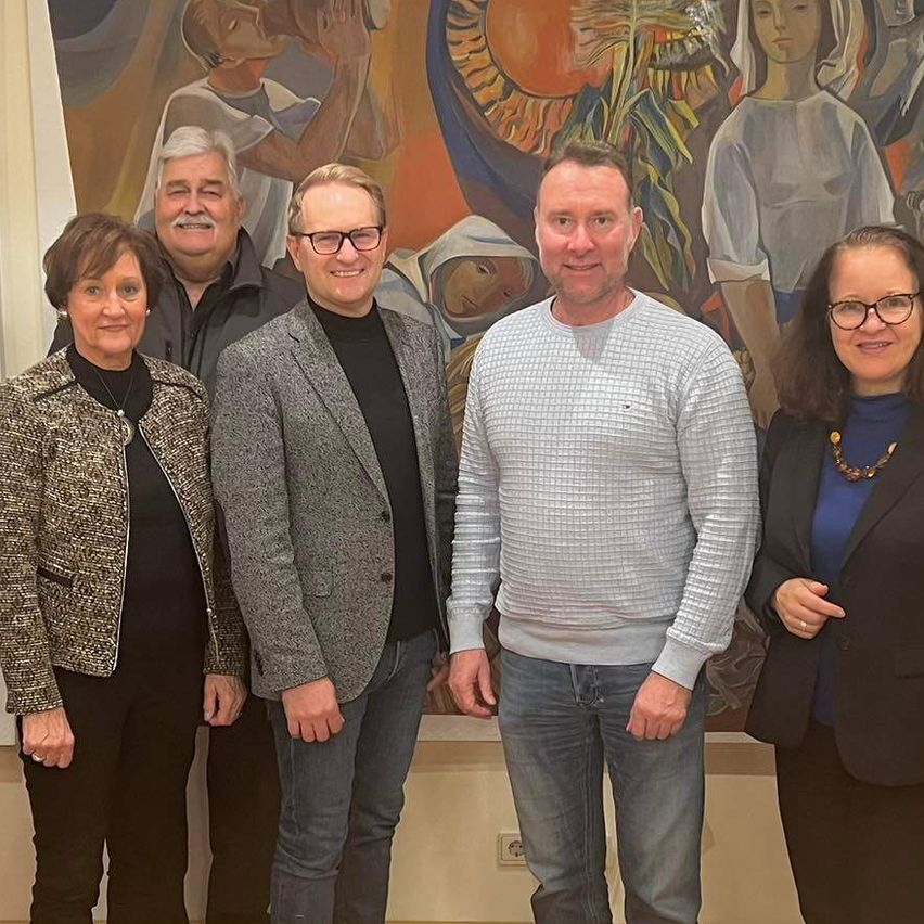 Eine Gruppe von Menschen steht lächelnd vor einer Wand mit großen Gemälden für ein Foto.