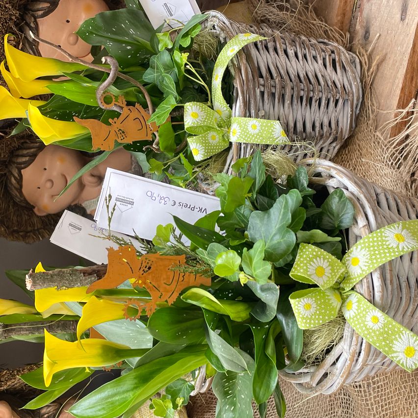 Nahaufnahme von zwei Weidenkörben gefüllt mit gelben Blumen und grünen Blättern mit Bändern und kleinen Karten.
