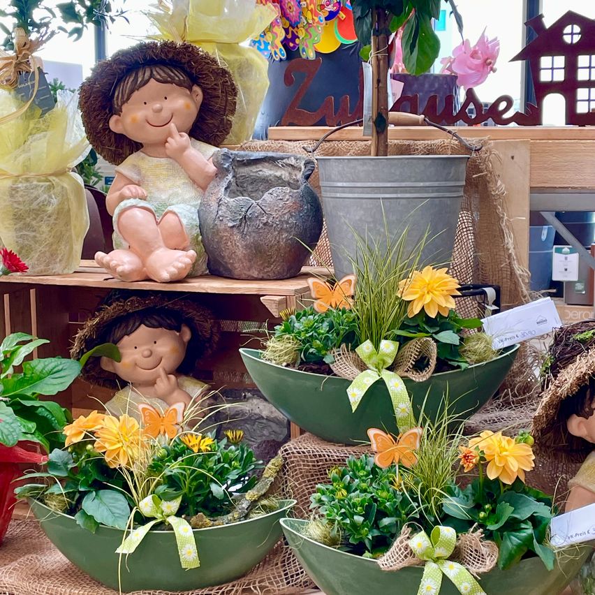 Eine Ausstellung von Blumenarrangements mit grünen Töpfen und gelben Blumen, begleitet von Figuren und Dekorationsartikeln auf Holzregalen.