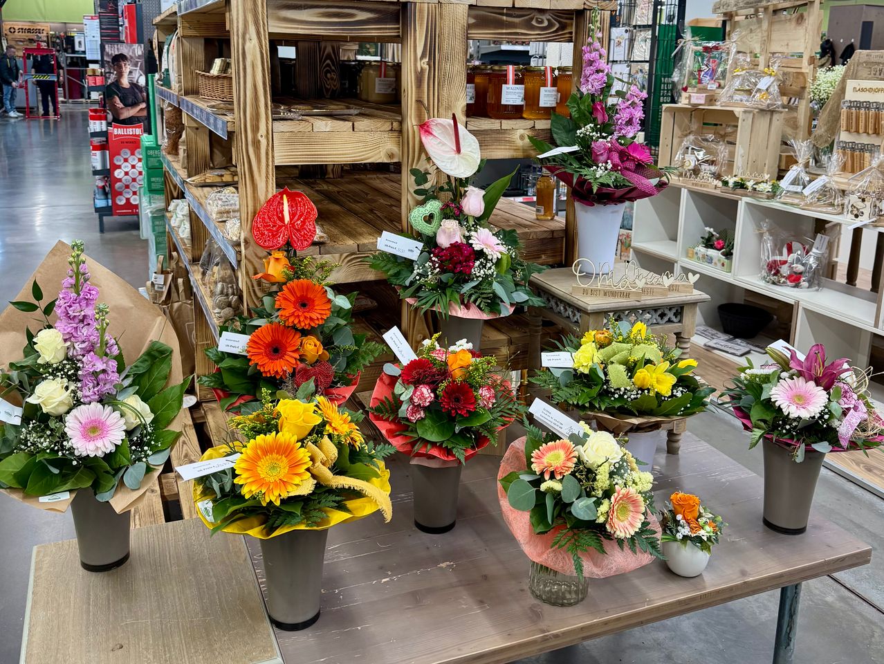Ein Blumenladen mit verschiedenen farbenfrohen Blumenarrangements in Glassvasen auf einem Holztisch, Holzregale im Hintergrund.