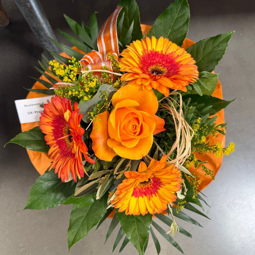An orange flower arrangement with a red rose and gerberas, adorned with green leaves and yellow flowers, tied with a ribbon.