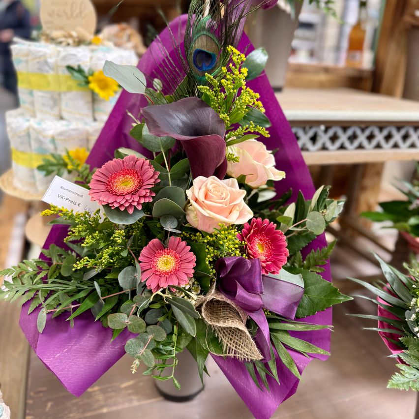 A bouquet with pink and white roses, green leaves, and purple wrapping is displayed in a store.