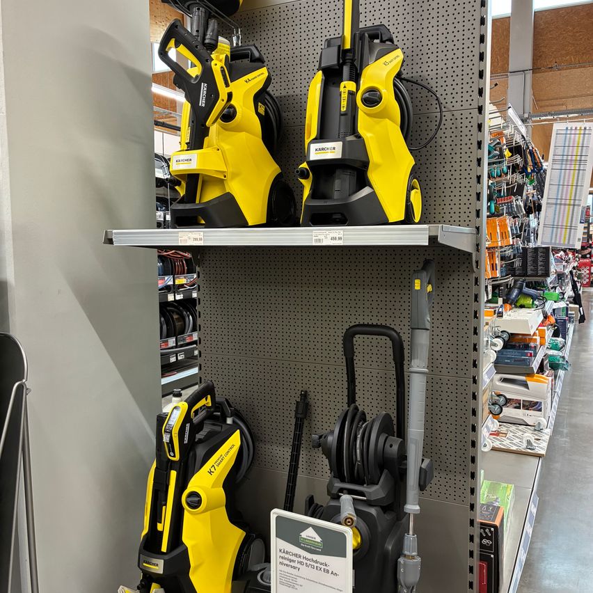 A store shelf displays yellow and black pressure washers. One has a price tag of 499.99 euros. The store is well-lit and organized.