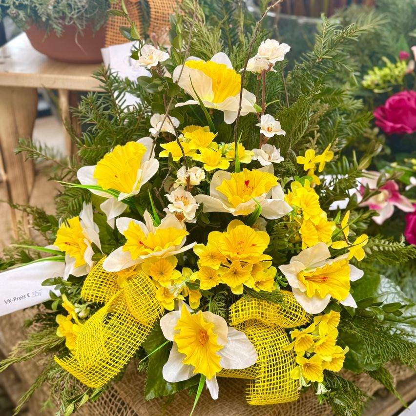 Eine lebhafte Blumenzusammenstellung mit gelben und weißen Narzissen, mit einem gelben Band gebunden, steht auf einem Holztisch mit Preisschild.