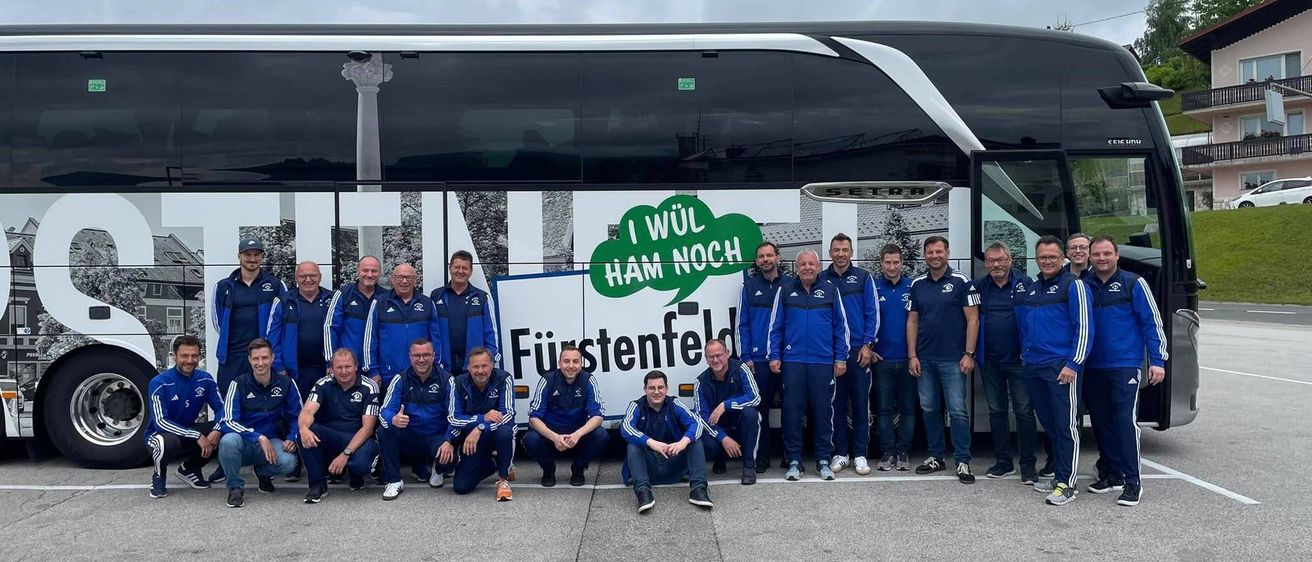 Ein Team in blauen Uniformen posiert vor einem Bus mit dem Slogan I WUL HAM NOCH FUIRSTENFELD.