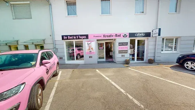 A pink car is parked outside a store with glass windows and a pink sign with the words Kreativ-Bad. A black car is parked on the right side.