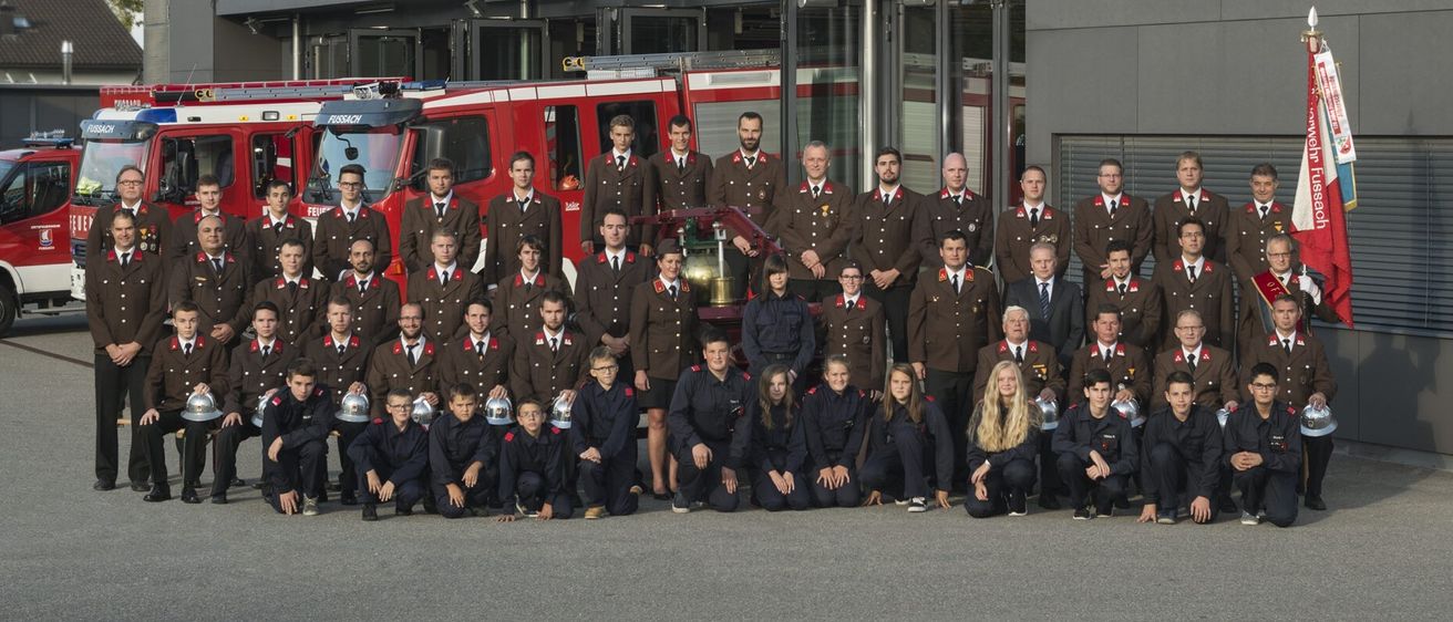Eine Gruppe Feuerwehrleute in Uniform, posiert für ein Foto vor einem Feuerwehrauto.
