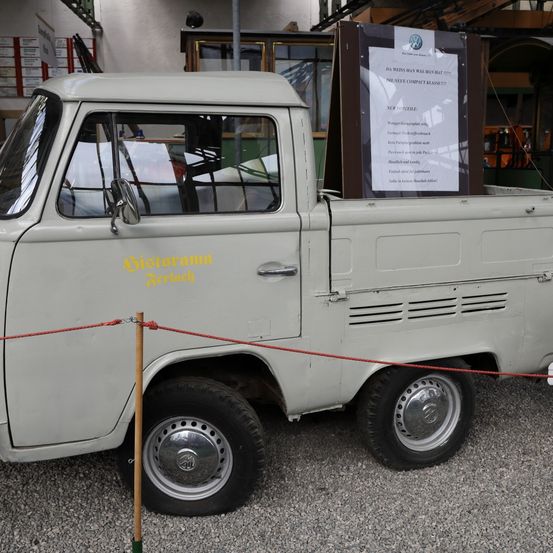 Ein weißer alter Volkswagen Pickup-Truck ist geparkt, mit einem Schild über seinem Laderaum, auf dem steht 'DA WEST MAN WAS MAN BEAT DIE NEXT COMPACT KLASSE 2017'. Der Truck hat gelben Text an der Seite und Chromfelgen.
