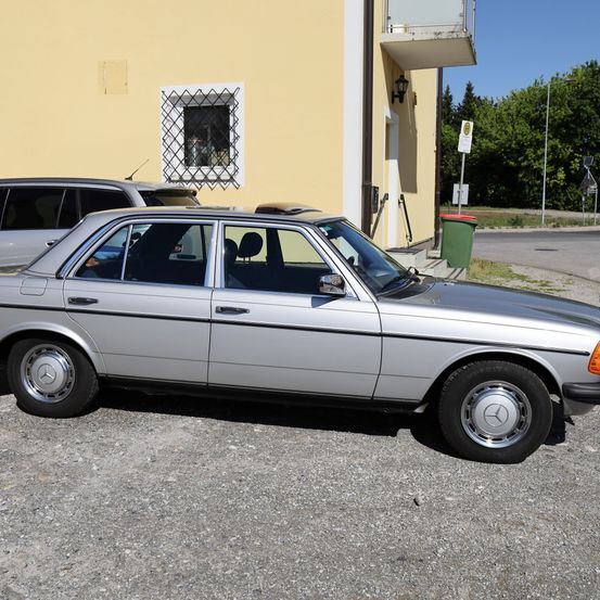 Ein silberner Mercedes Benz Sedan vor einem gelben Gebäude mit Balkon geparkt.