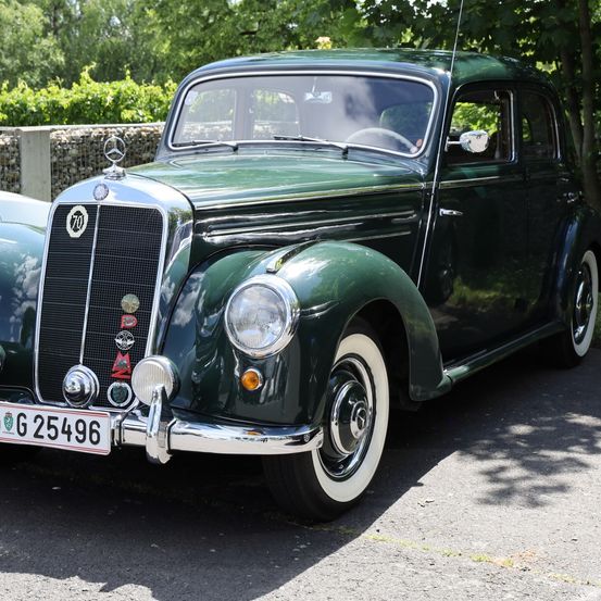 Ein altes grünes Auto mit dem Kennzeichen G 25496 ist auf einem Rasen geparkt. Das Auto hat weiße Räder und einen silbernen Stoßfänger.