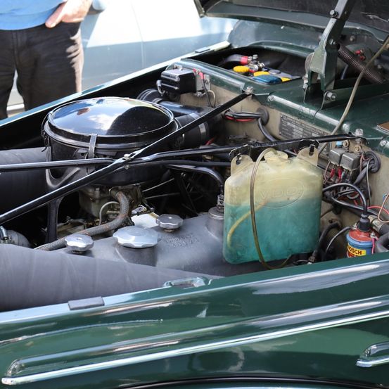 Ein geöffneter grüner Automotor mit sichtbaren Teilen. Ein Mann steht dahinter, gekleidet in Blau.