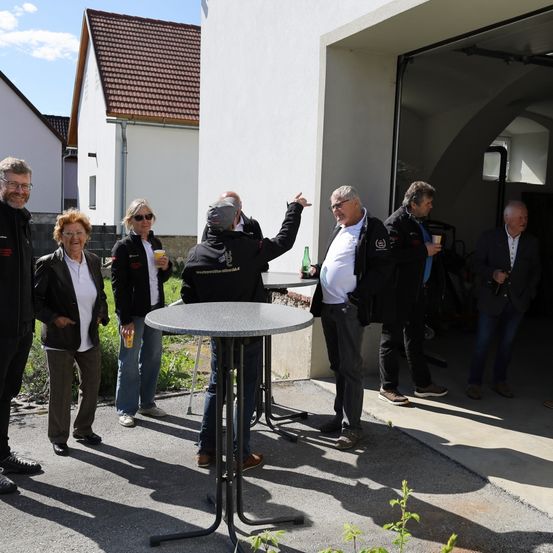Mehrere Personen in Jacken stehen um einen Tisch herum im Freien. Ein Mann zeigt auf etwas. Sie halten wahrscheinlich eine Besprechung ab.