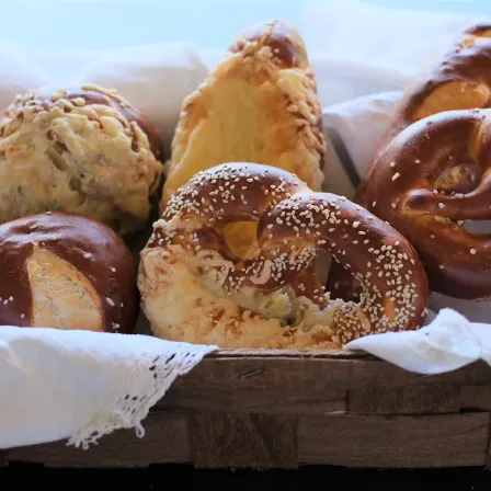 Ein Holzkorb gefüllt mit verschiedenen Brezelsorten. Eine hat Sesam, während die anderen verschiedene Beläge haben.