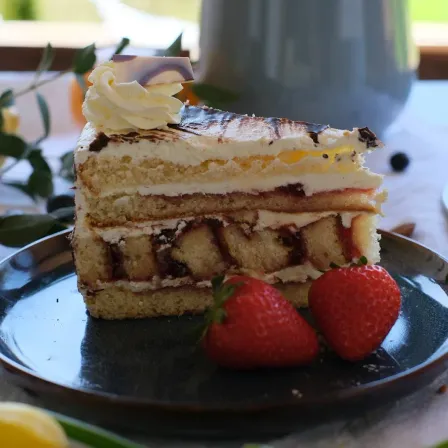 Ein Stück mehrschichtiger Kuchen mit Sahne, Erdbeere und Schokolade auf einem Teller mit zwei Erdbeeren. Im Hintergrund befindet sich ein Tisch mit einer Vase und Pflanzen.