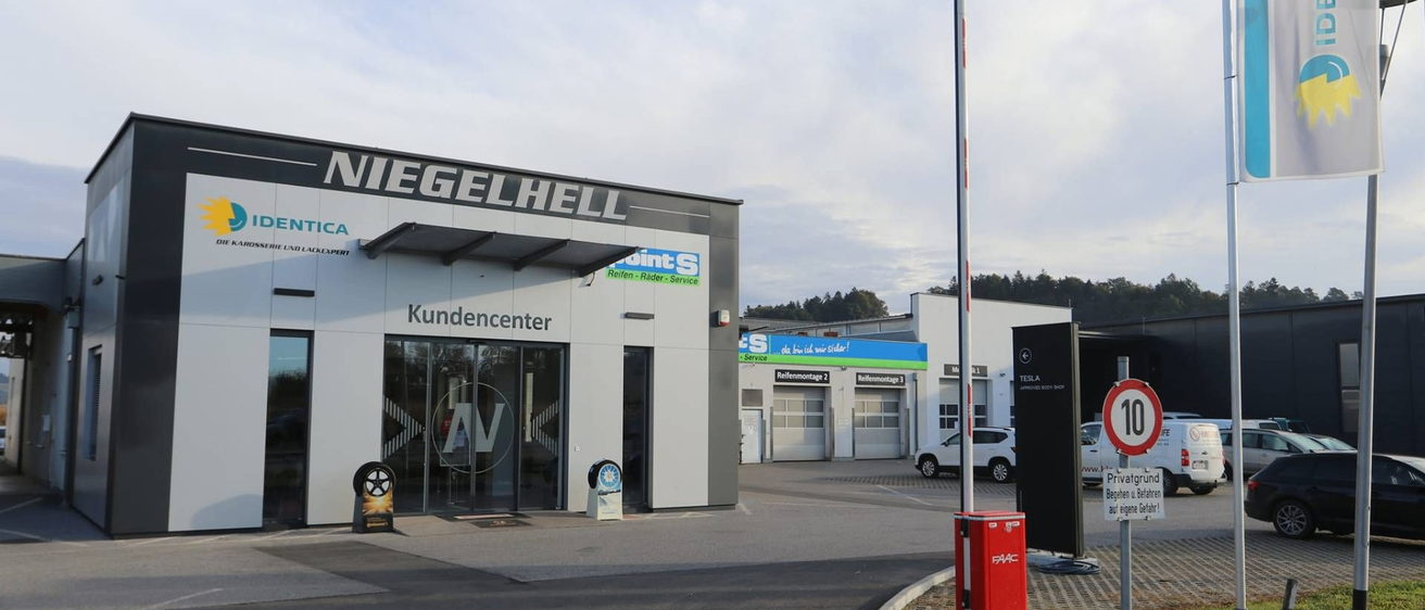 Die Vorderseite eines modernen Gebäudes mit einem Schild, das Niegelhell liest, mit einem Kundencenter-Eingang, großen Glastüren und einem weißen Auto, das in der Nähe geparkt ist.