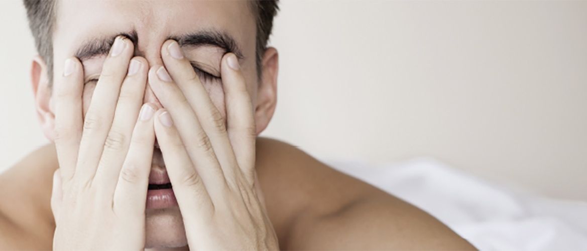 Ein Mann liegt auf einem Bett mit geschlossenen Augen und bedecktem Gesicht, sieht erschöpft aus.