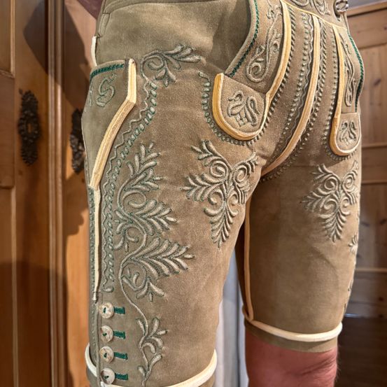 Nahaufnahme traditioneller deutscher Lederhosen mit aufwendiger Stickerei und dekorativen Details an den Gesäßtaschen und Knöpfen.