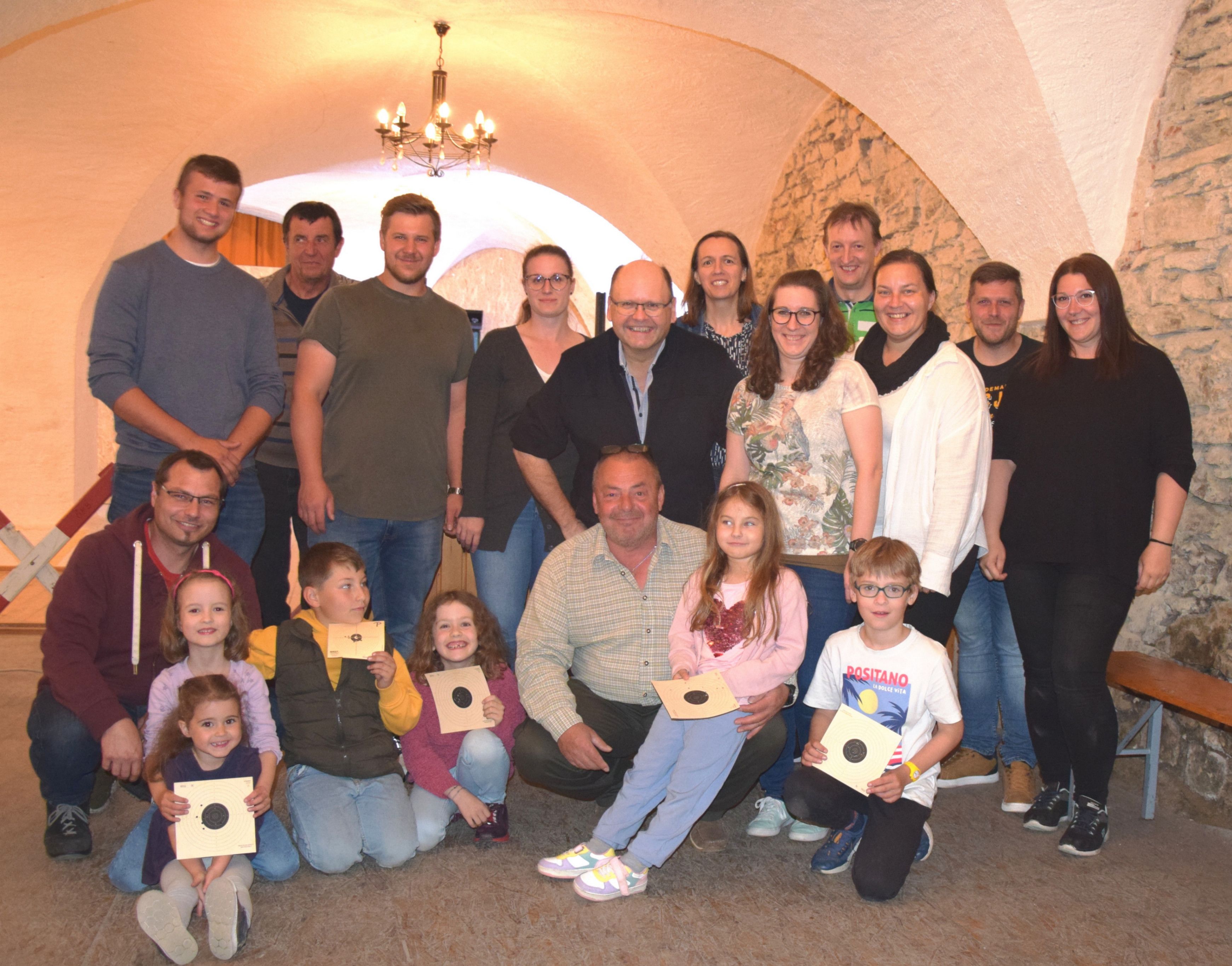 Eine Gruppe von Menschen posiert für ein Foto in einem gewölbten Raum. Einige halten Urkunden. Eine Laterne hängt von der Decke, und die Wände sind aus Stein.