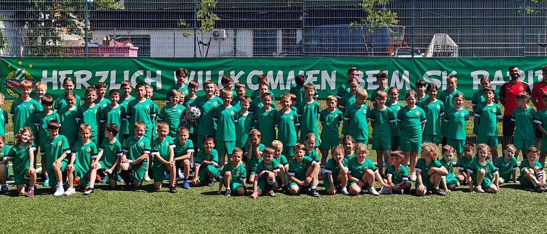Eine Gruppe junger Fußballspieler in grünen Trikots posiert für ein Foto vor einem grünen Banner.
