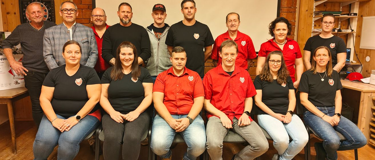 Eine Gruppe von Personen in roten und schwarzen Hemden und Jeans posiert für ein Foto, wahrscheinlich für ein Team- oder Firmenbild.
