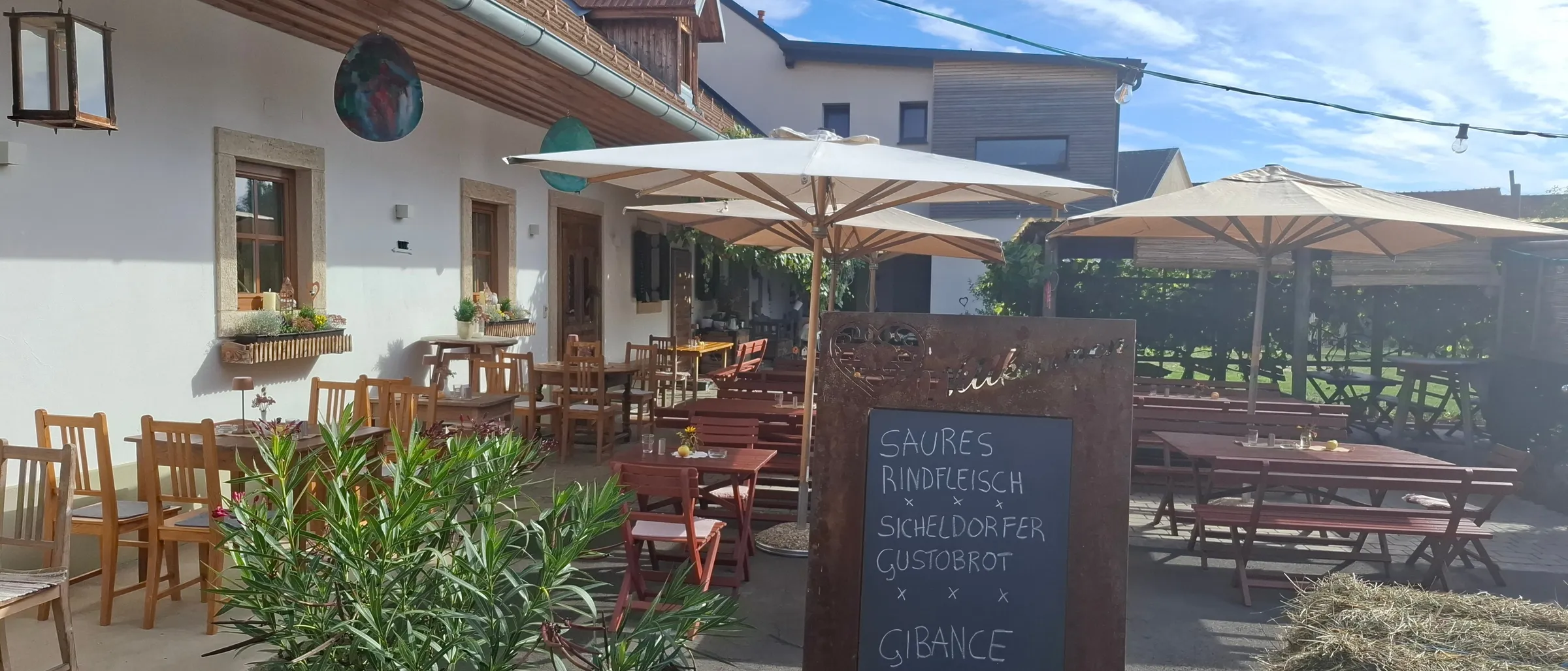 Ein Restaurant mit Sitzgelegenheiten im Freien unter Sonnenschirmen. Ein Kreidetafelmenü wird angezeigt.