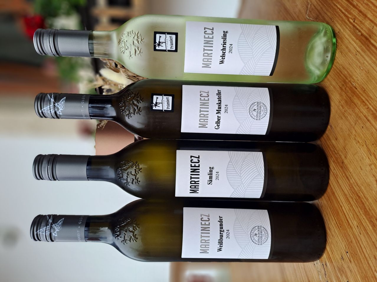 Vier Weinflaschen sind auf einer Holzoberfläche ausgestellt. Die oberste Flasche ist klar, gefolgt von drei grünen Flaschen. Die Etiketten tragen den Namen Martinec und Jahrgangsdaten.