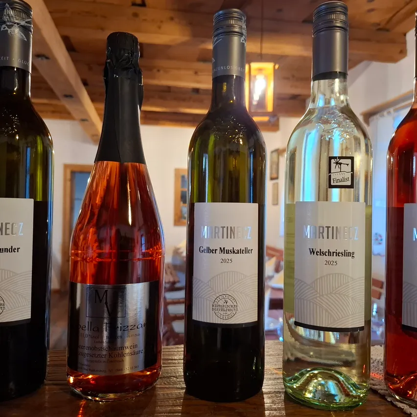 Fünf Flaschen Wein sind auf einem Holztisch aufgereiht. Die Flaschen sind in verschiedenen Farben und Größen und jede hat ein Etikett mit dem Namen des Weins und dem Jahr, in dem er produziert wurde.
