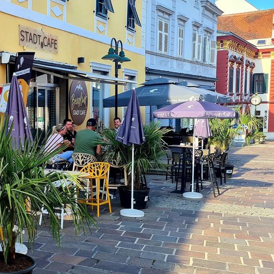 Outdoor seating at a cafe called Stadt Cafe with several people sitting under umbrellas on a brick patio.